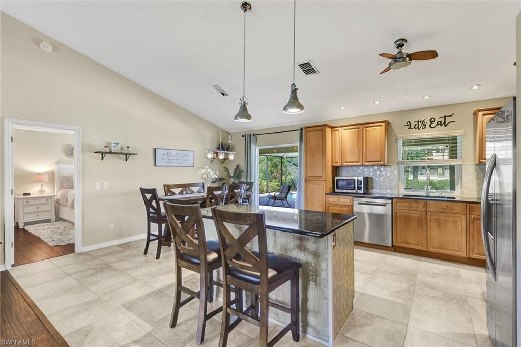 Kitchen with a breakfast bar area, ceiling fan, wood finish cabinetry, stainless steel appliances, and vaulted ceiling
