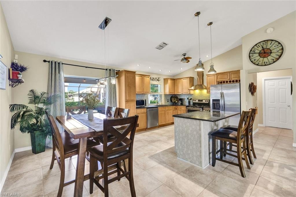 Kitchen featuring lofted ceiling, a center island, stainless steel appliances, decorative light fixtures, and a kitchen breakfast bar