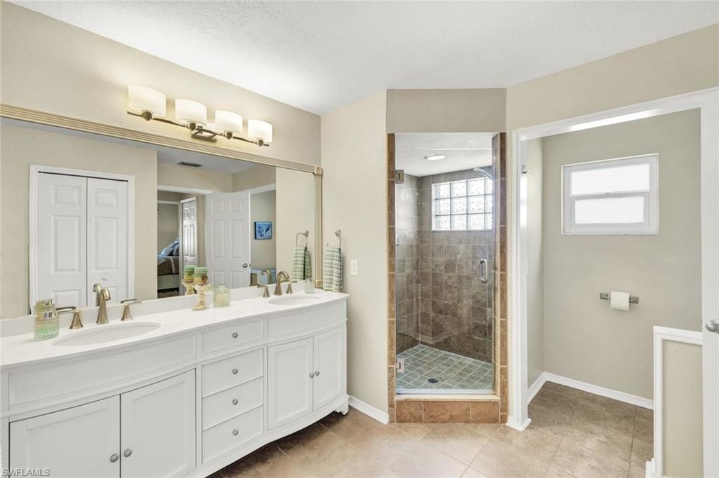 Full bath with double vanity, a shower stall, a closet, and light tile patterned floors