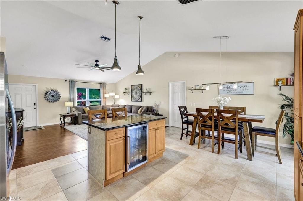 Kitchen with pendant lighting, dark stone counters, open floor plan, wine cooler, and light tile patterned flooring