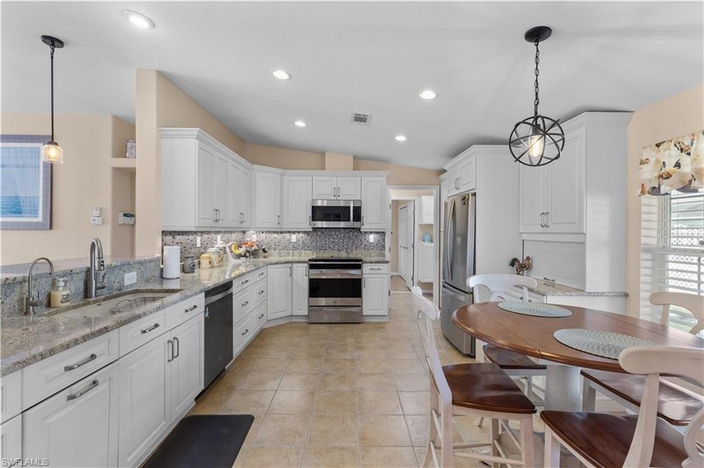 Kitchen featuring hanging light fixtures, light stone counters, stainless steel appliances, white cabinets, and lofted ceiling