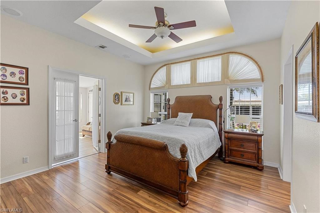 Bedroom featuring ceiling fan, light wood-style flooring, and a tray ceiling