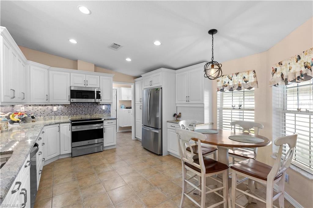Kitchen with lofted ceiling, stainless steel appliances, white cabinets, light stone countertops, and tasteful backsplash