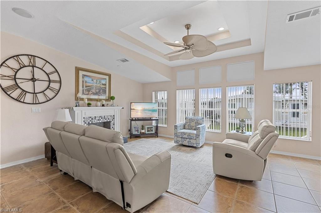 Living area with a fireplace, ceiling fan, a tray ceiling, light tile patterned floors, and recessed lighting
