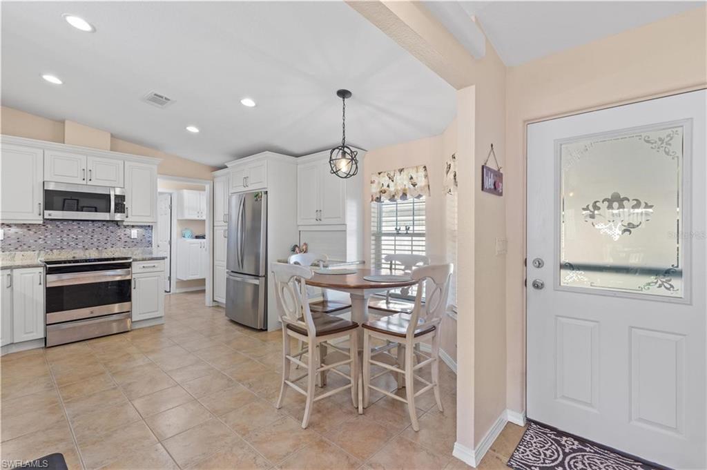 Kitchen with stainless steel appliances, white cabinetry, backsplash, light stone countertops, and hanging light fixtures