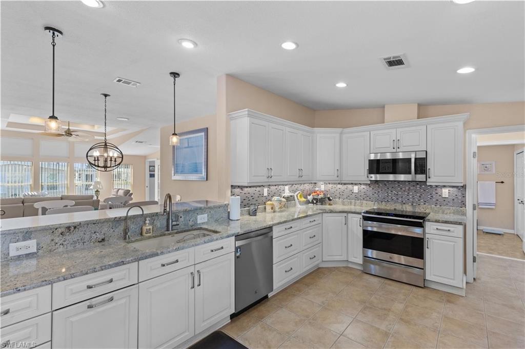 Kitchen featuring stainless steel appliances, white cabinetry, light stone countertops, and open floor plan