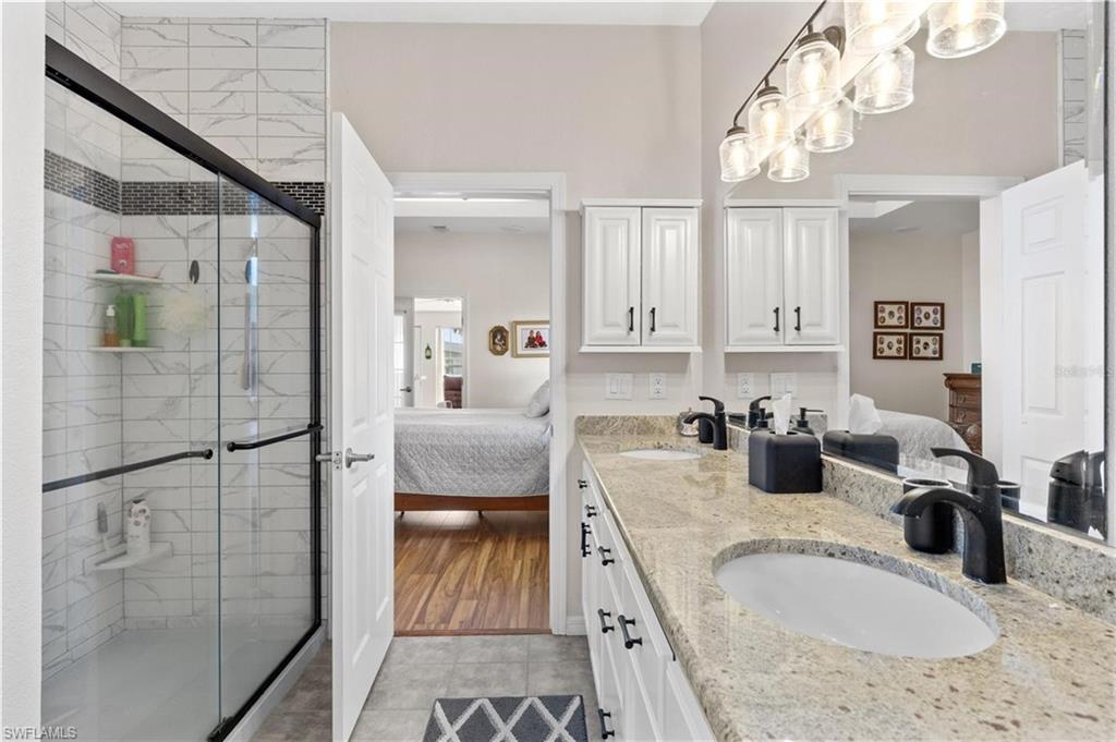 Bathroom with connected bathroom, double vanity, a stall shower, and light tile patterned flooring