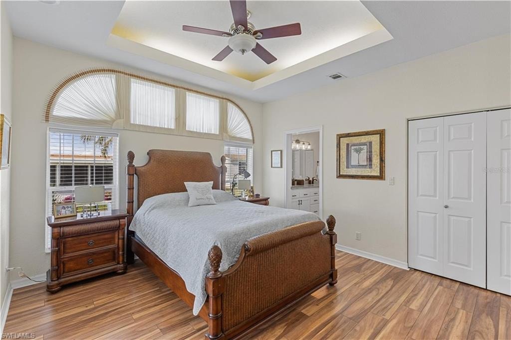 Bedroom with ceiling fan, wood finished floors, connected bathroom, a closet, and a raised ceiling