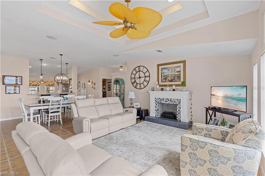 Tiled living area with a tiled fireplace, ceiling fan, a chandelier, and a tray ceiling