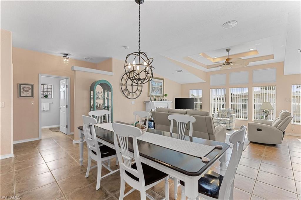 Dining area featuring a tray ceiling, ceiling fan, light tile patterned floors, and a chandelier