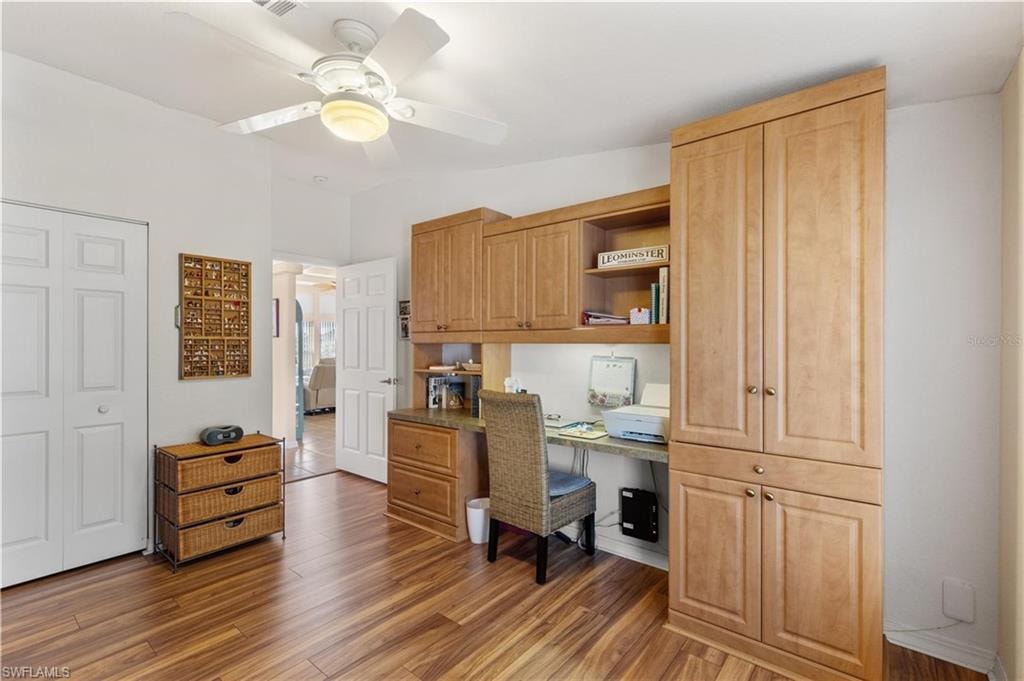 Office space featuring built in desk, a ceiling fan, and dark wood-type flooring