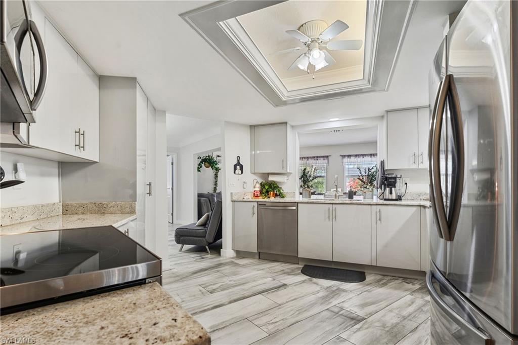 Kitchen with stainless steel appliances, light stone counters, ceiling fan, ornamental molding, and white cabinets