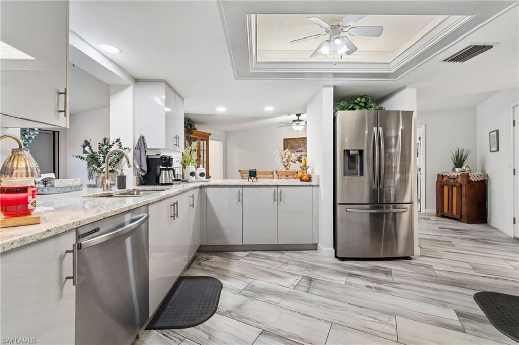Kitchen featuring stainless steel appliances, light stone counters, ornamental molding, a ceiling fan, and a peninsula