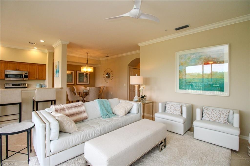 Living area featuring ceiling fan with notable chandelier, visible vents, arched walkways, and ornamental molding