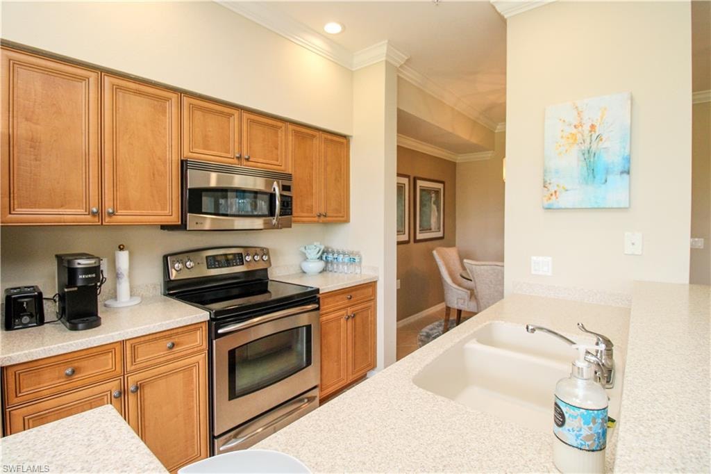 Kitchen with light countertops, ornamental molding, appliances with stainless steel finishes, a sink, and brown cabinetry
