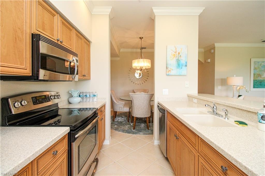 Kitchen with ornamental molding, a sink, a notable chandelier, and appliances with stainless steel finishes