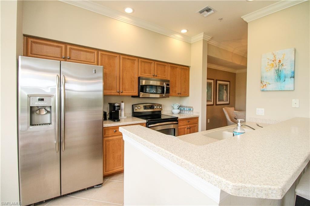 Kitchen featuring light tile patterned floors, stainless steel appliances, visible vents, a peninsula, and brown cabinets