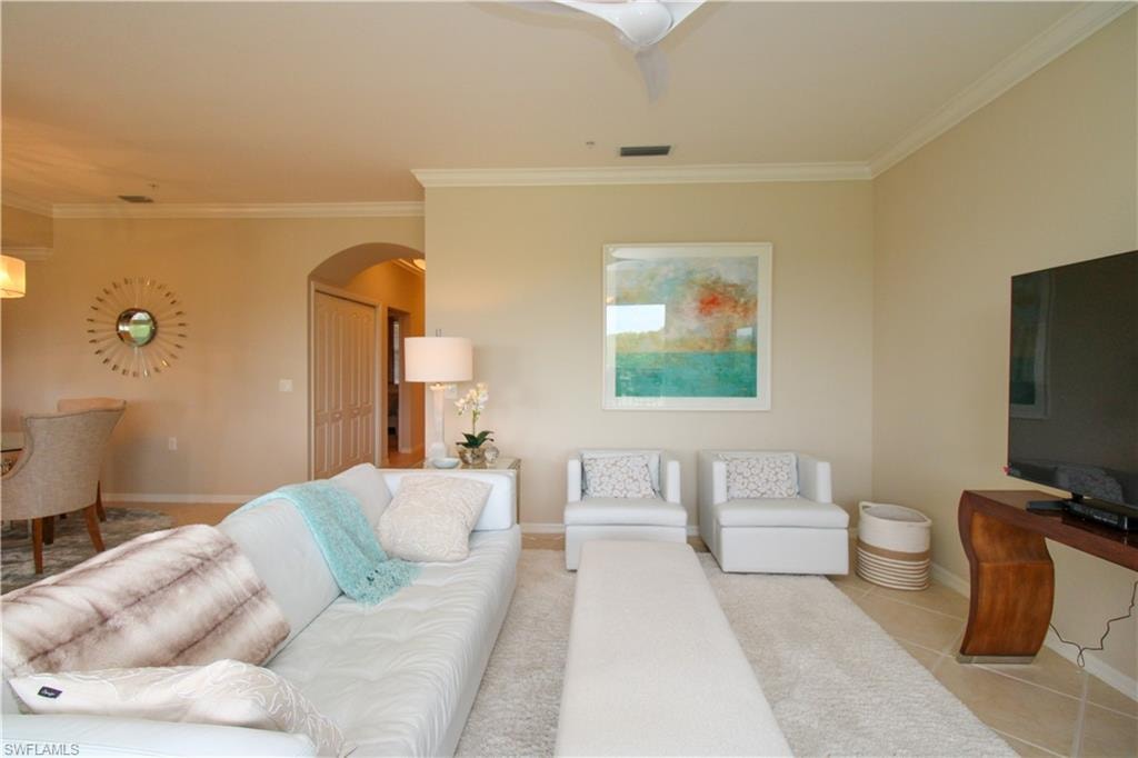 Tiled living room featuring arched walkways, baseboards, ornamental molding, and visible vents