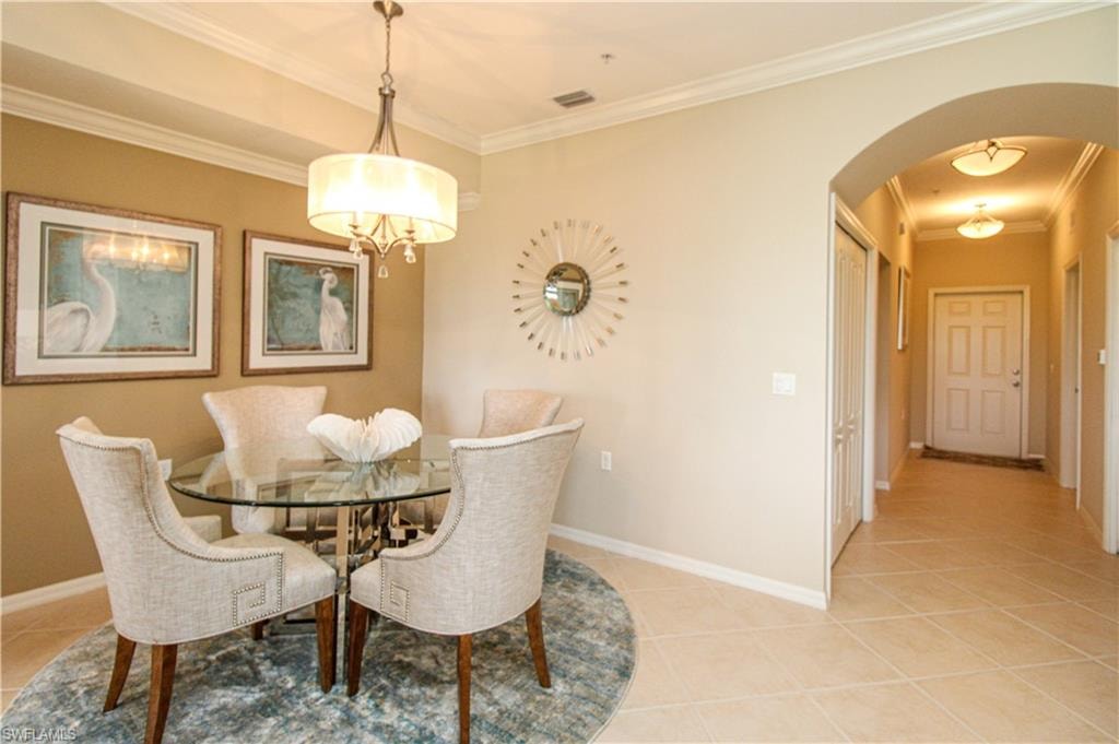 Dining room featuring light tile patterned flooring, visible vents, baseboards, ornamental molding, and arched walkways