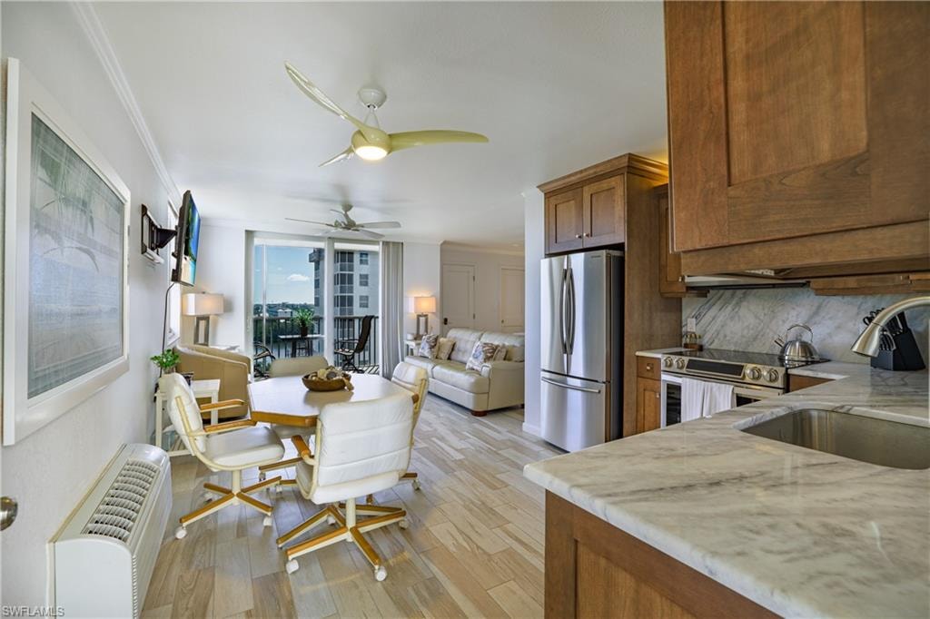 Kitchen with stainless steel appliances, wood finish cabinetry, light wood-style flooring, open floor plan, and light stone countertops