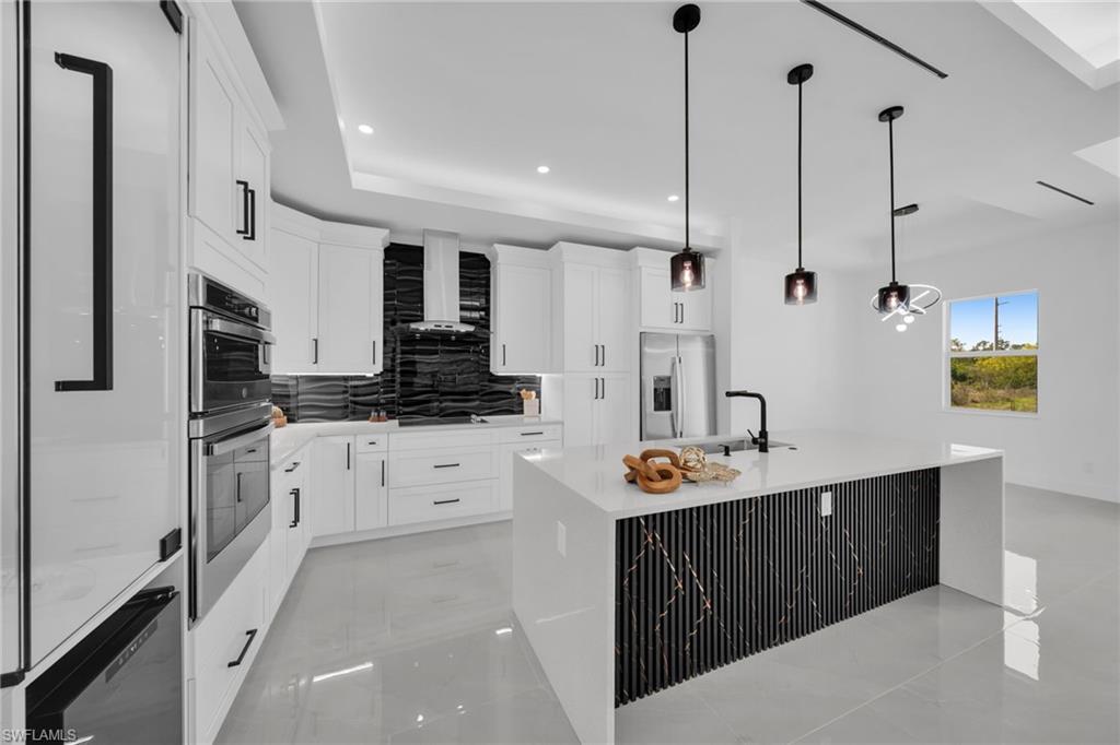 Kitchen featuring a kitchen island with sink, decorative backsplash, light stone counters, stainless steel appliances, and white cabinets