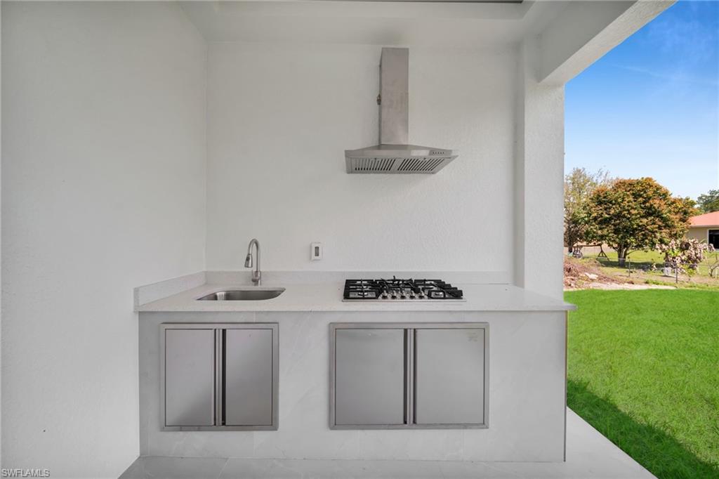 Kitchen with wall chimney exhaust hood, light stone counters, and stainless steel gas cooktop