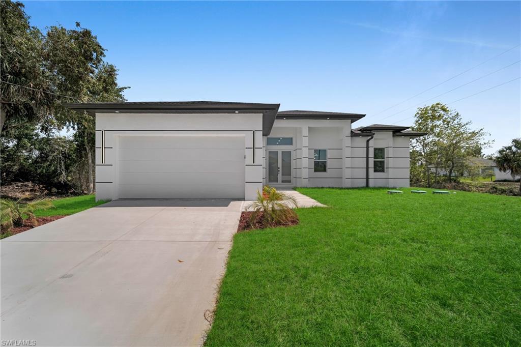 View of front of property with an attached garage, driveway, a front yard, and stucco siding