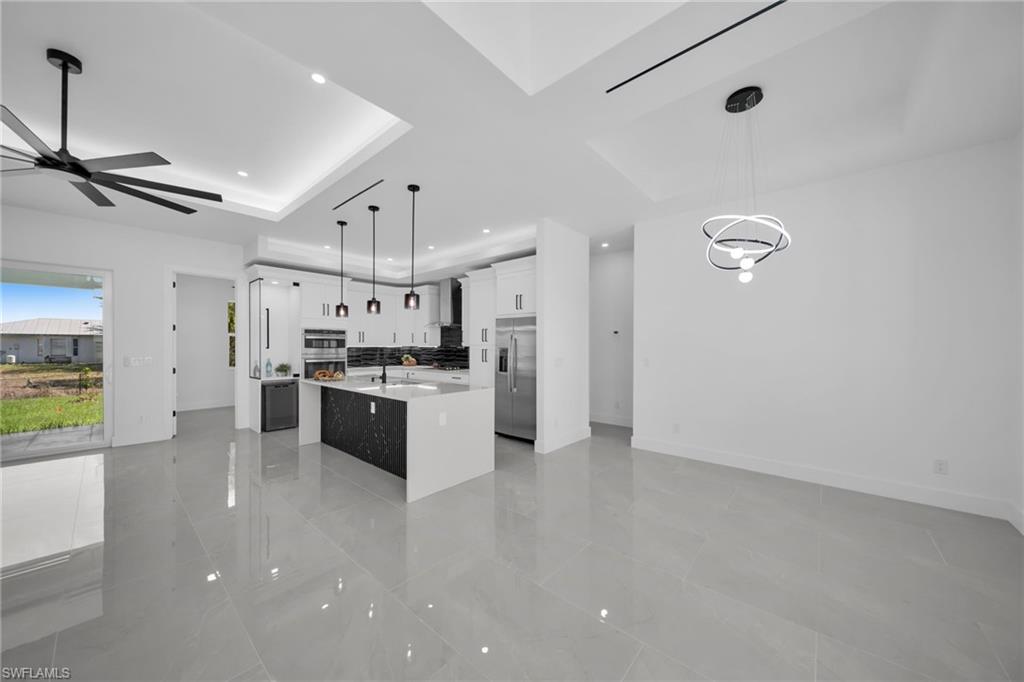 Kitchen featuring an island with sink, decorative light fixtures, white cabinets, light stone counters, and open floor plan