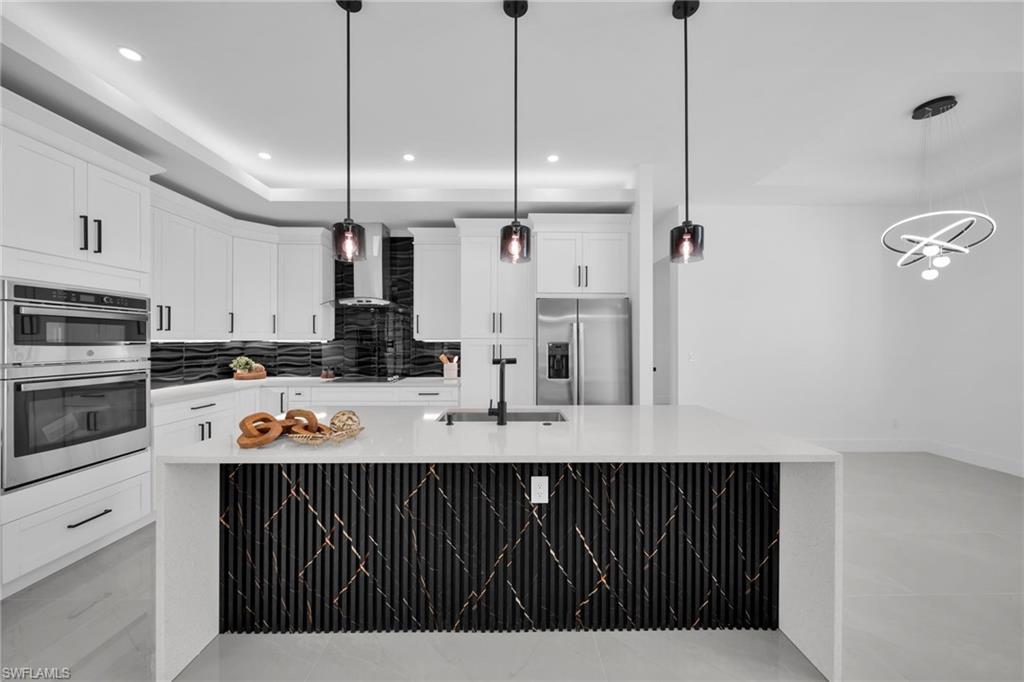 Kitchen with stainless steel appliances, backsplash, white cabinetry, a large island with sink, and light stone countertops