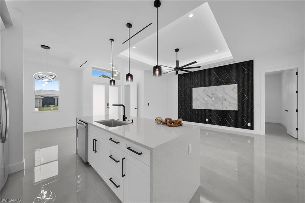 Kitchen featuring an accent wall, white cabinetry, a raised ceiling, a center island with sink, and light stone countertops