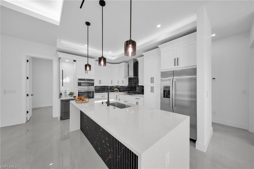 Kitchen featuring light stone countertops, stainless steel appliances, a center island with sink, backsplash, and white cabinets