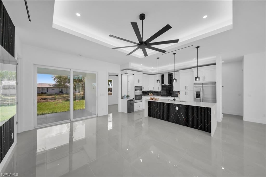Kitchen with white cabinets, a large island, stainless steel appliances, hanging light fixtures, and light stone counters