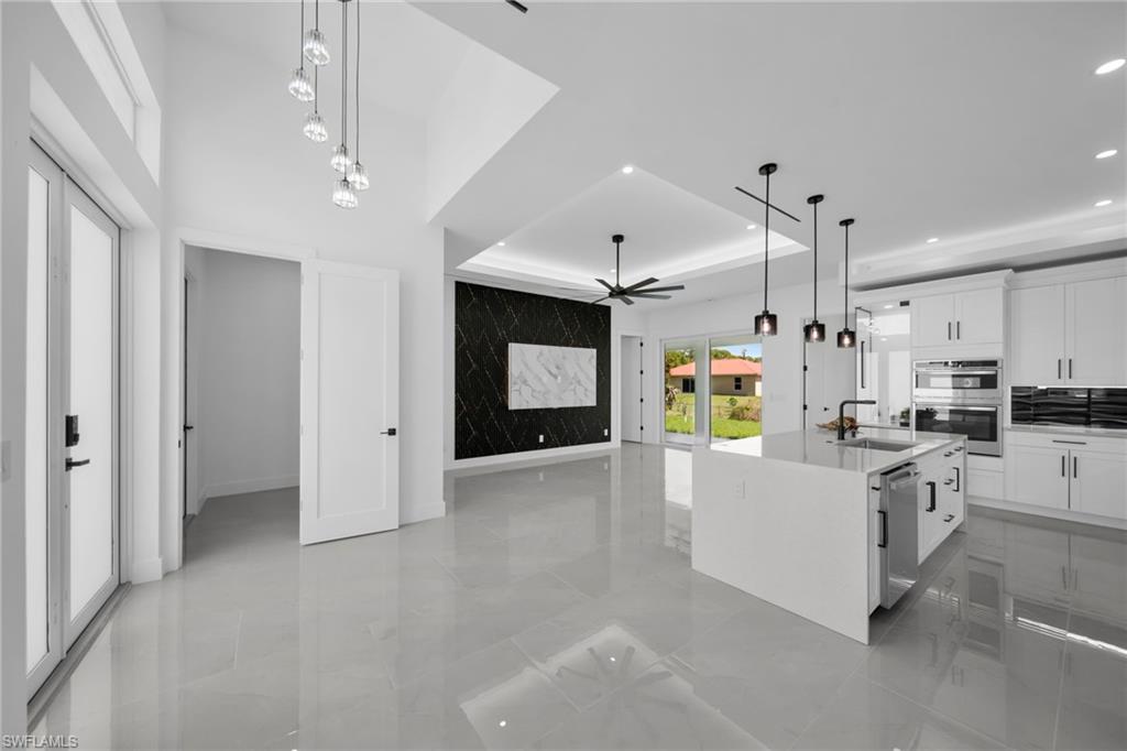 Kitchen with white cabinets, an island with sink, a tray ceiling, hanging light fixtures, and light stone counters