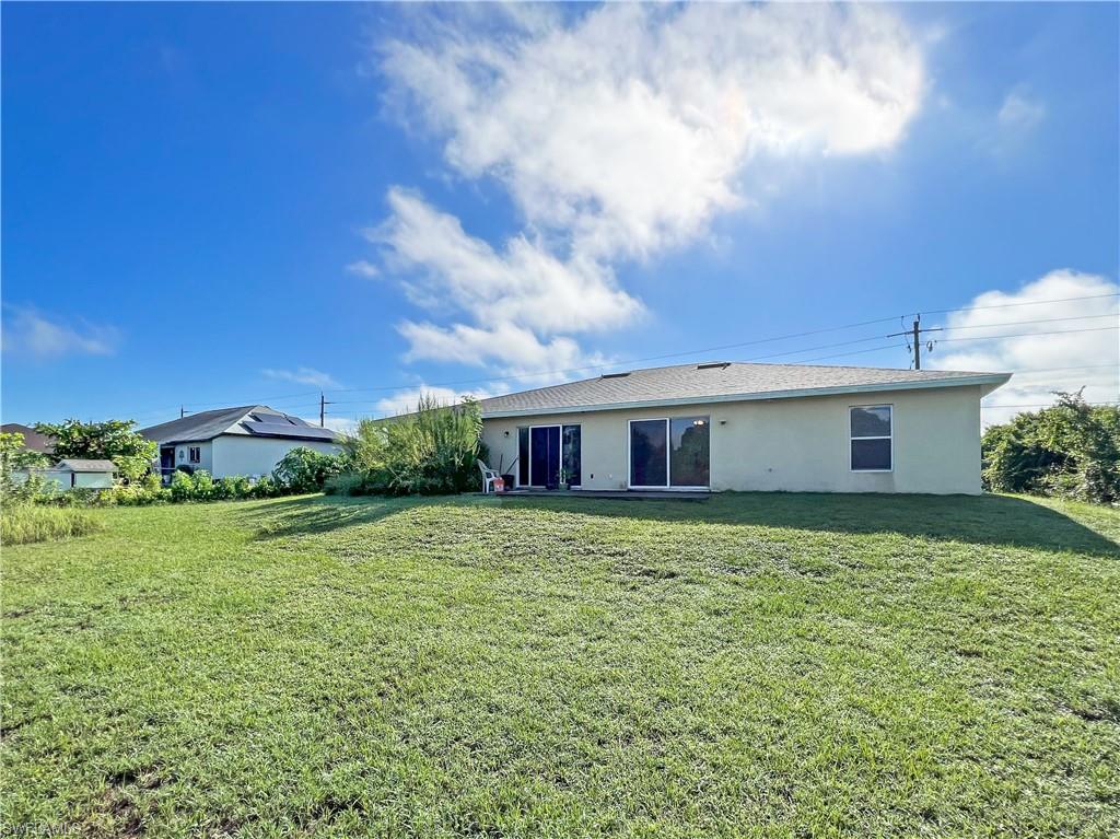Back of property with a lawn and stucco siding