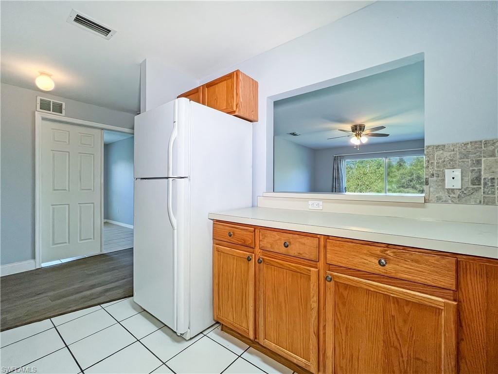 Kitchen featuring freestanding refrigerator, light countertops, wood finish cabinets, and light tile patterned floors