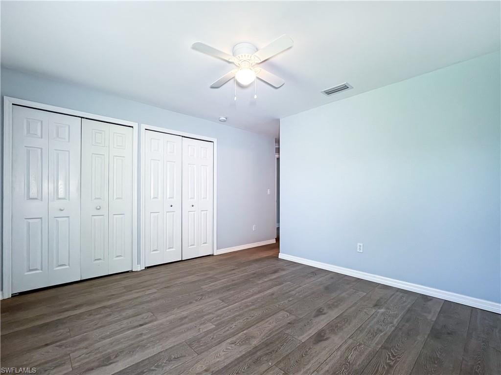 Unfurnished bedroom featuring multiple closets, a ceiling fan, and dark wood-type flooring