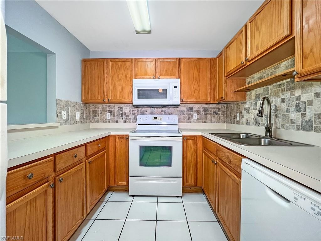 Kitchen featuring white appliances, wood finish cabinetry, light countertops, and light tile patterned floors