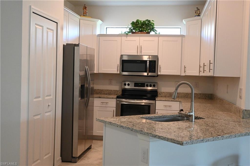 Kitchen with white cabinetry, stainless steel appliances, light stone countertops, and a peninsula