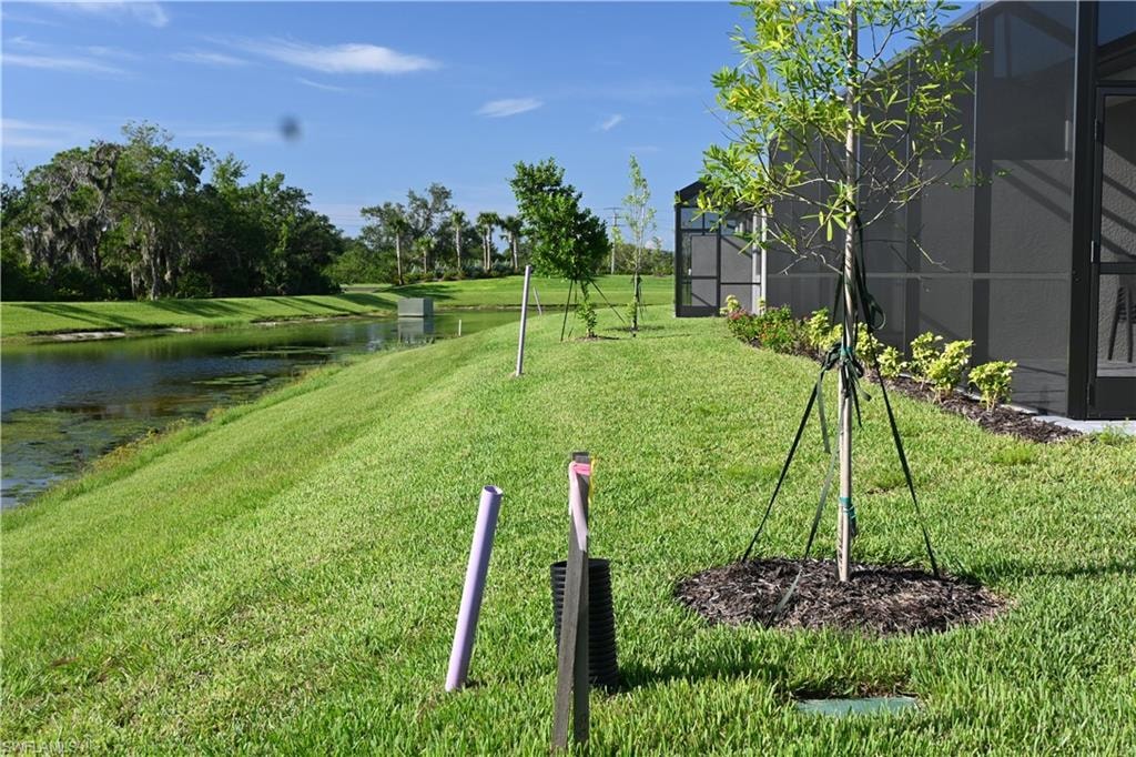 View of grassy yard featuring a lanai, a water view, and a sunroom