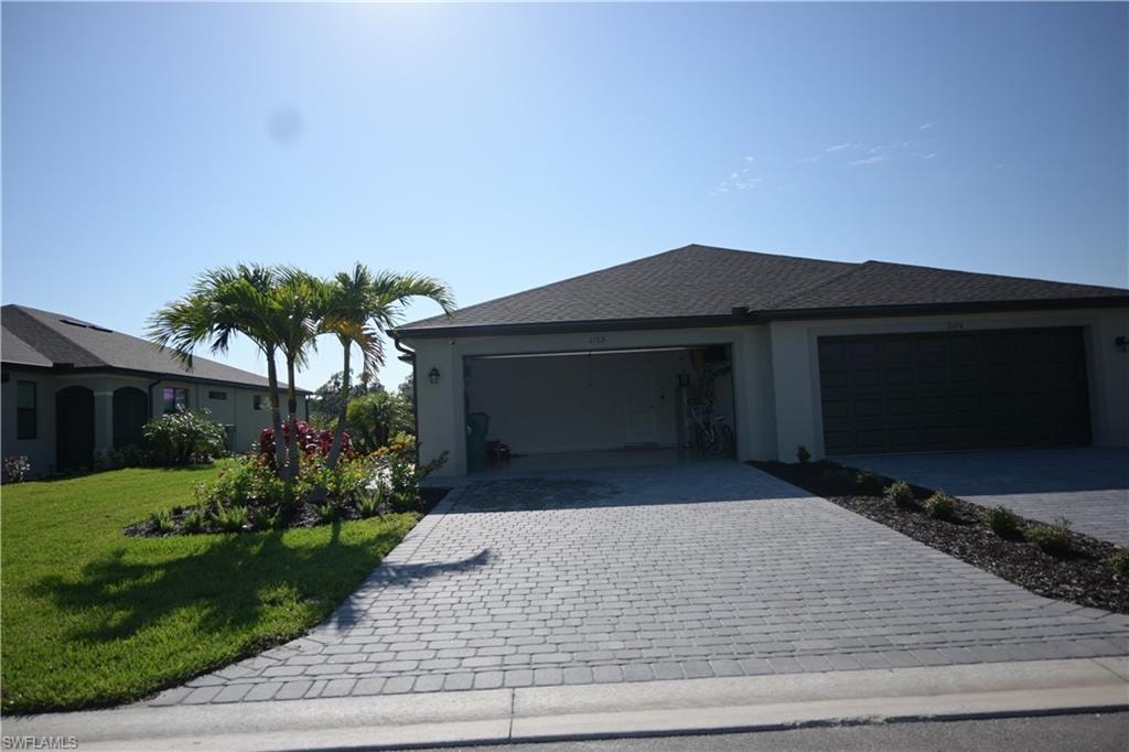 View of front of home with decorative driveway, stucco siding, roof with shingles, and a front lawn