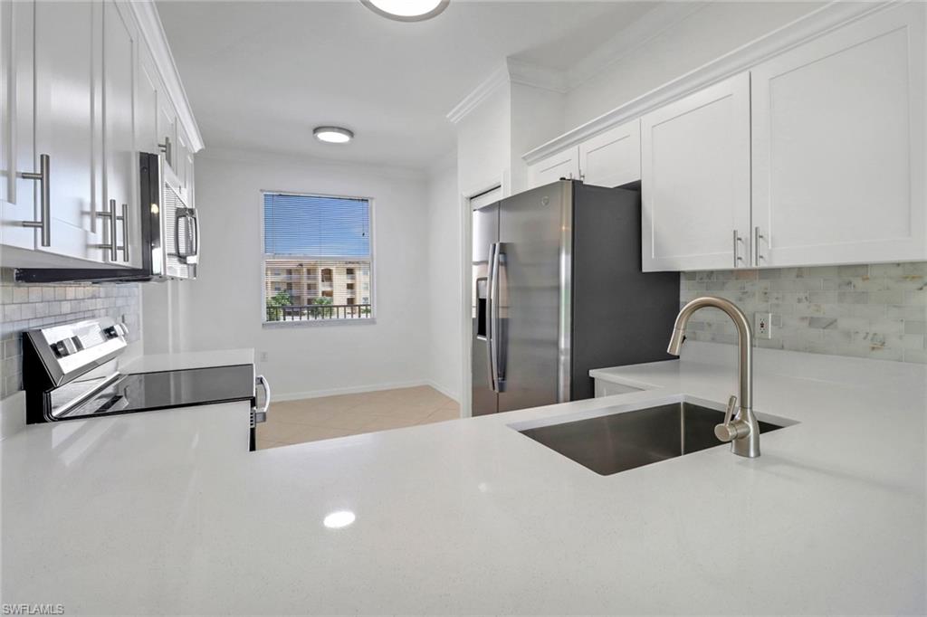 Kitchen with appliances with stainless steel finishes, tasteful backsplash, white cabinets, sink, and light tile patterned floors