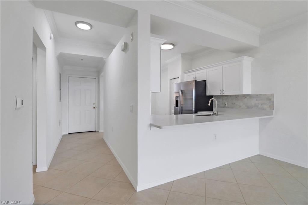 Kitchen featuring white cabinets, stainless steel fridge, sink, and light tile patterned floors