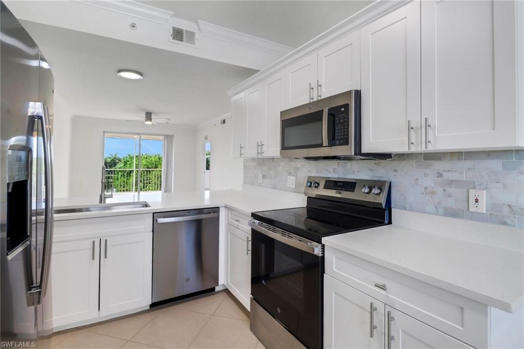Kitchen featuring appliances with stainless steel finishes, white cabinets, sink, kitchen peninsula, and ornamental molding