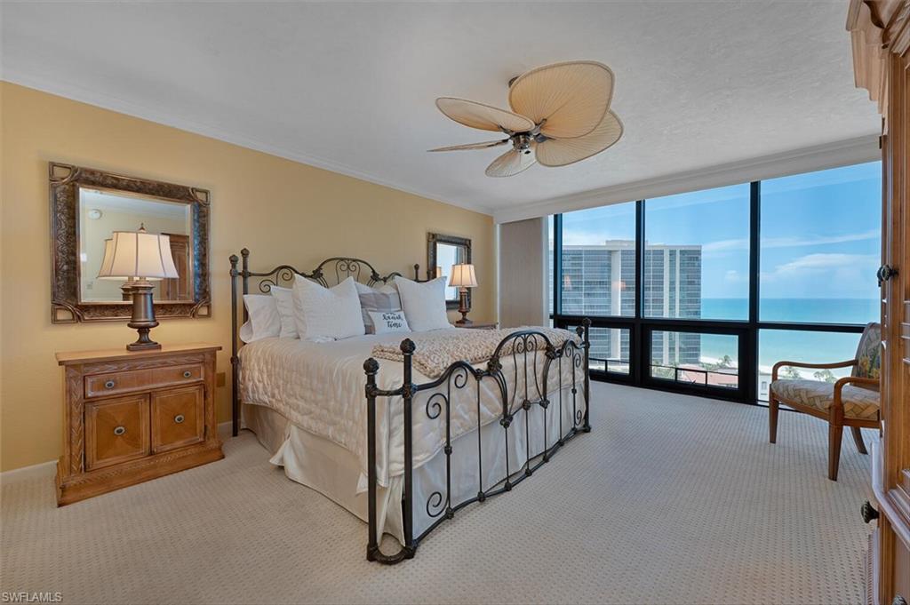 Carpeted bedroom featuring expansive windows, a ceiling fan, ornamental molding, a water view, and a view of city