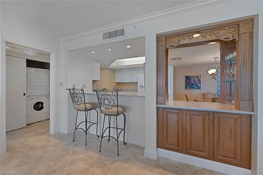 Kitchen with a kitchen breakfast bar, stacked washing machine and dryer, crown molding, white refrigerator with ice dispenser, and light stone counters