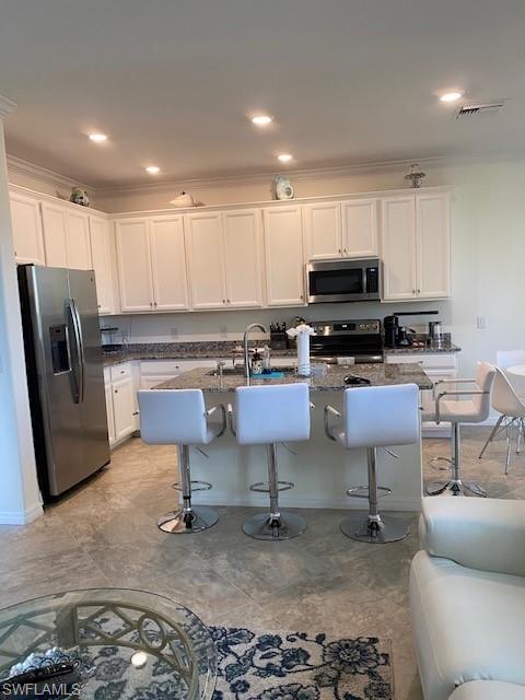 Kitchen featuring a kitchen island with sink, dark stone countertops, white cabinets, a breakfast bar, and appliances with stainless steel finishes