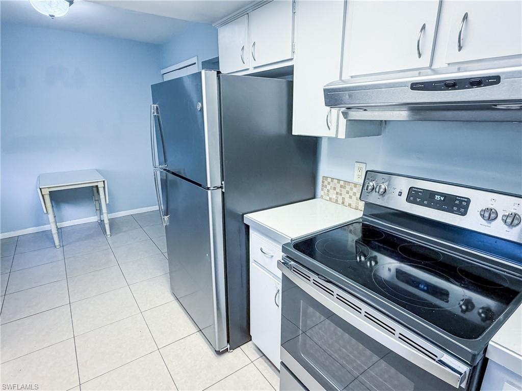 Kitchen with stainless steel appliances, light countertops, white cabinetry, and light tile patterned floors