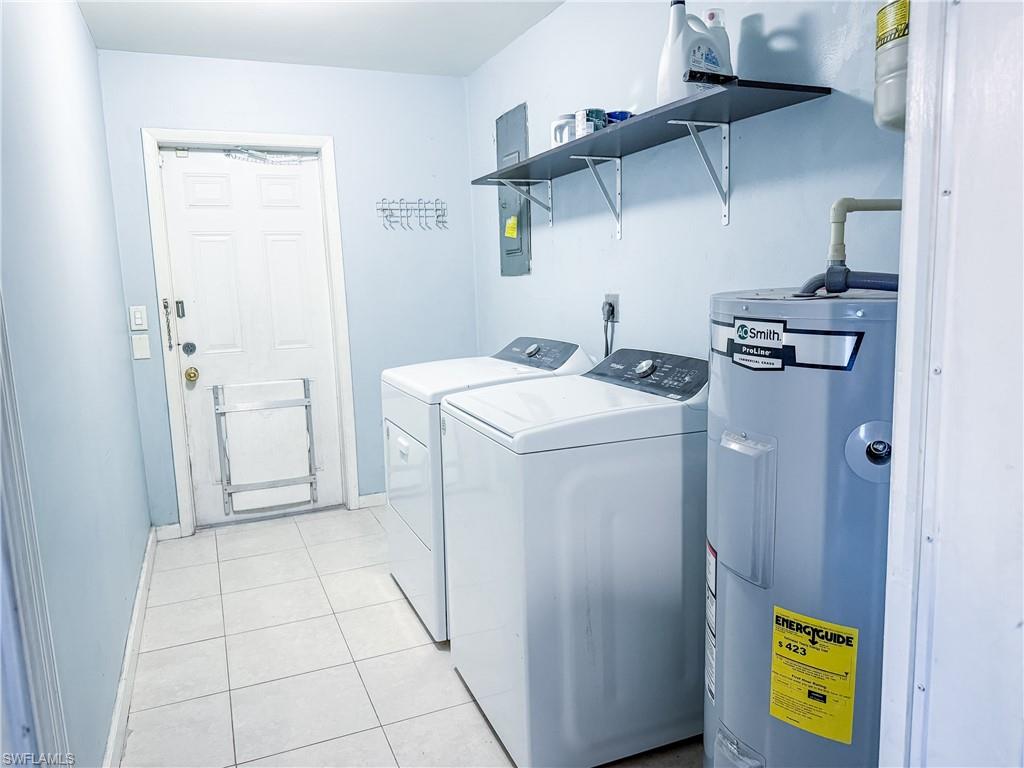 Laundry area featuring water heater, light tile patterned floors, washer and dryer, and door leading to the backyard.