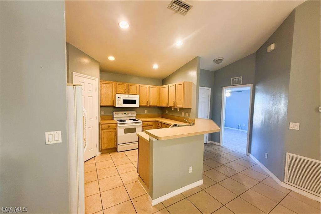 Kitchen featuring white appliances, light countertops, a peninsula, lofted ceiling, and light tile patterned floors