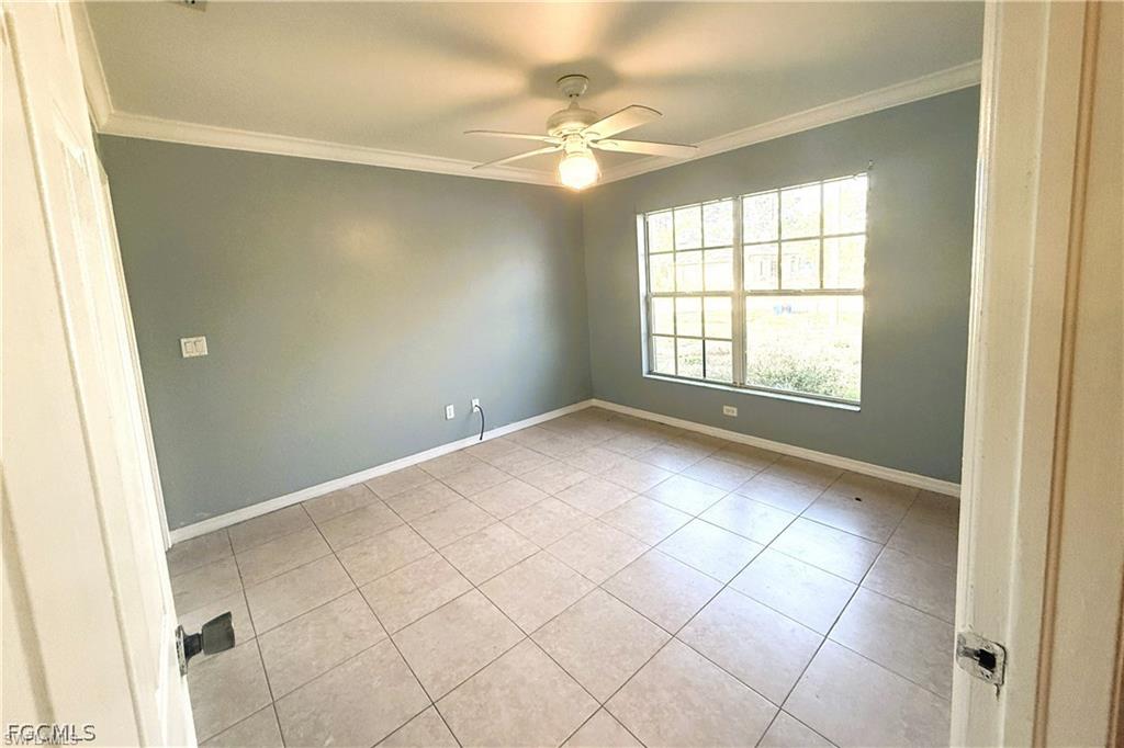 Empty room featuring crown molding, ceiling fan, and light tile patterned floors